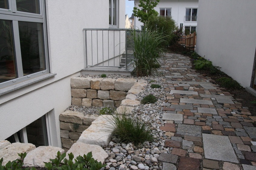 Lichtschacht aus Jura Kalkstein, Kiesbeet mit Gr&auml;sern und Weg mit einem gemischten bunten Pflaster.  (M&uuml;nchen)