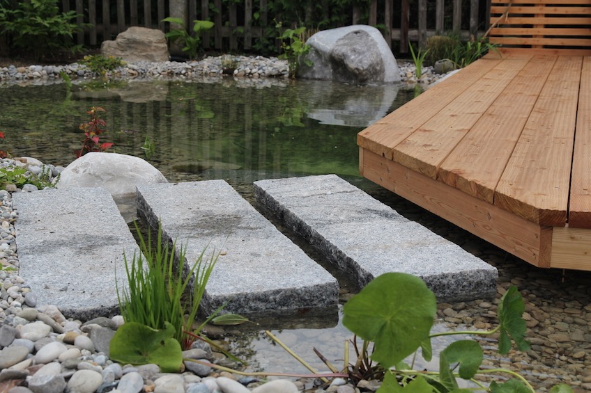 Flach gelegte Granit Randsteine dienen als Weg übers Wasser auf das Holzdeck. (München)