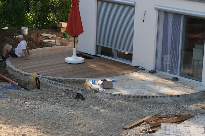 Runde Holzterrasse mit Einfassung aus Granit Großstein, die von einer Steinterrasse mit Belag aus Quarzit angeschnitten wird. (Deisenhofen - Oberhaching)