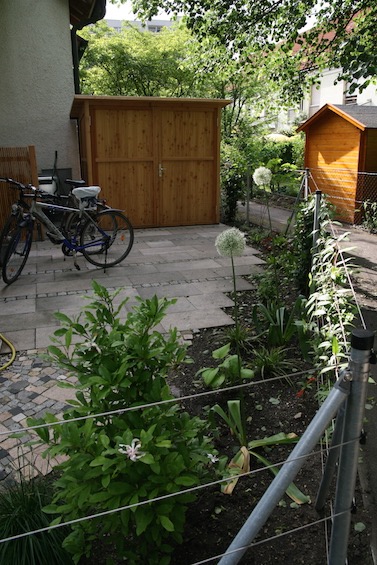Fahrradstellplatz mit den alten Terrassenplatten aus Waschbeton und einzelnen Streifen mit Granit Kleinstein. Gartenschrank nach Maß der Firma Scholbeck. (Garching bei München)