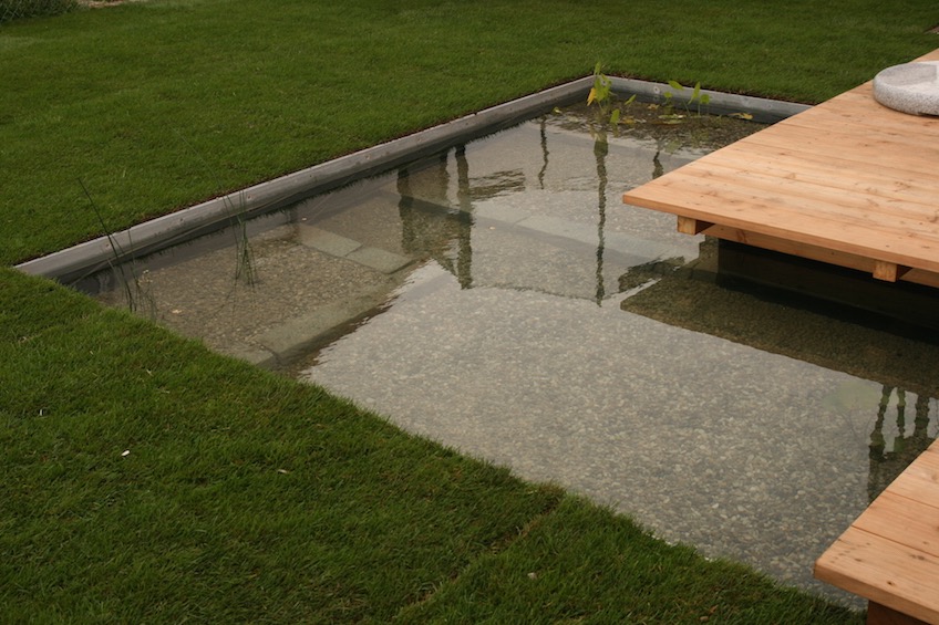 Mit Stahlkanten gefasste formale Wasserfläche und über das Wasser ragendes Holzdeck. (Poing bei München)