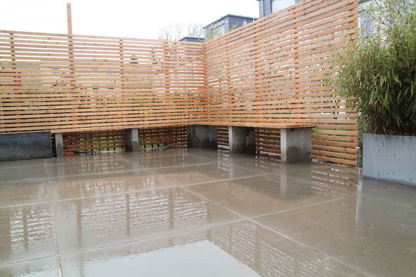 Terrasse mit großformatigen Betonplatten, Sichtschutz aus Holz und Bank mit Sitzauflage aus Holz. (Freising)